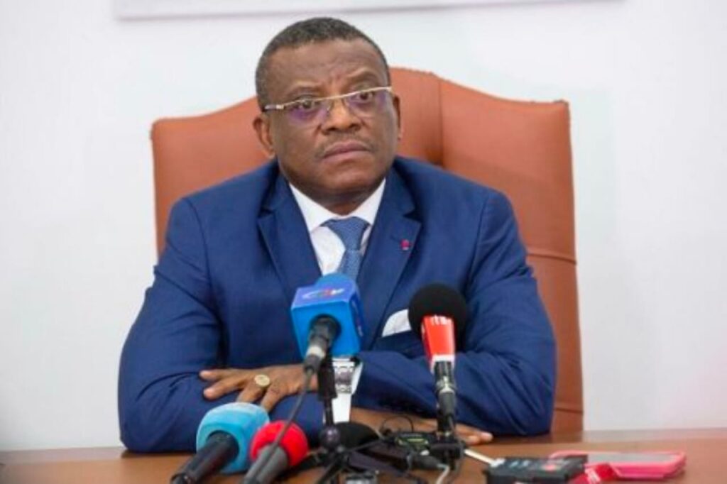 Dr David Makongo seated behind microphones, wearing a blue suit.
