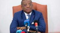 Dr David Makongo seated behind microphones, wearing a blue suit.