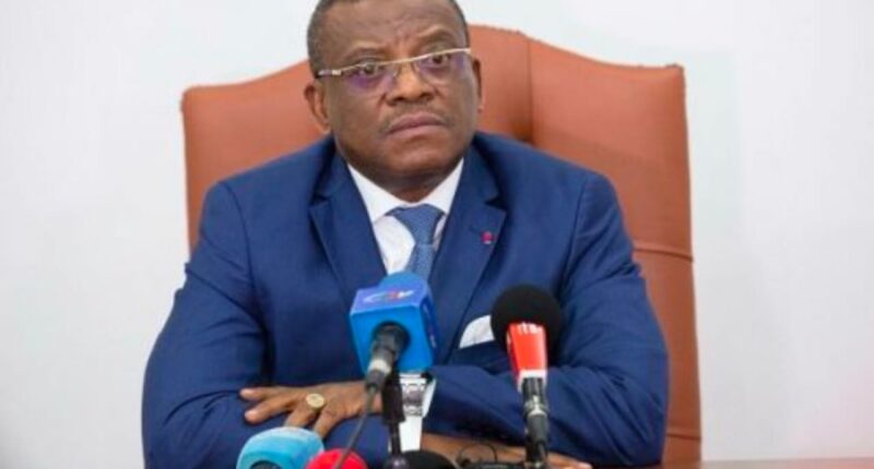 Dr David Makongo seated behind microphones, wearing a blue suit.