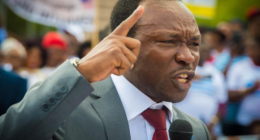 Ayaba Cho Lucas speaking into a microphone with his index finger raised.