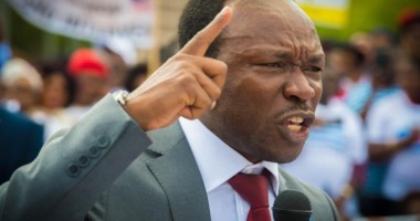 Ayaba Cho Lucas speaking into a microphone with his index finger raised.
