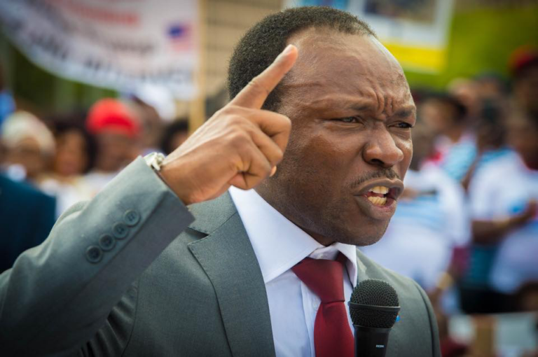 Ayaba Cho Lucas speaking into a microphone with his index finger raised.