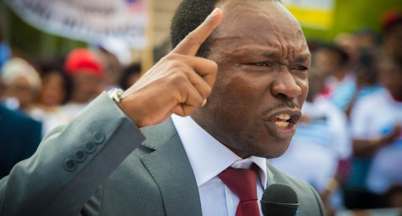 Ayaba Cho Lucas speaking into a microphone with his index finger raised.